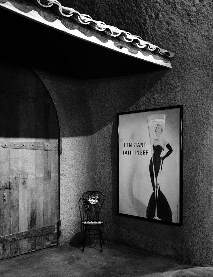 Taittinger poster near metal chair and wooden door on B. Wise Estate