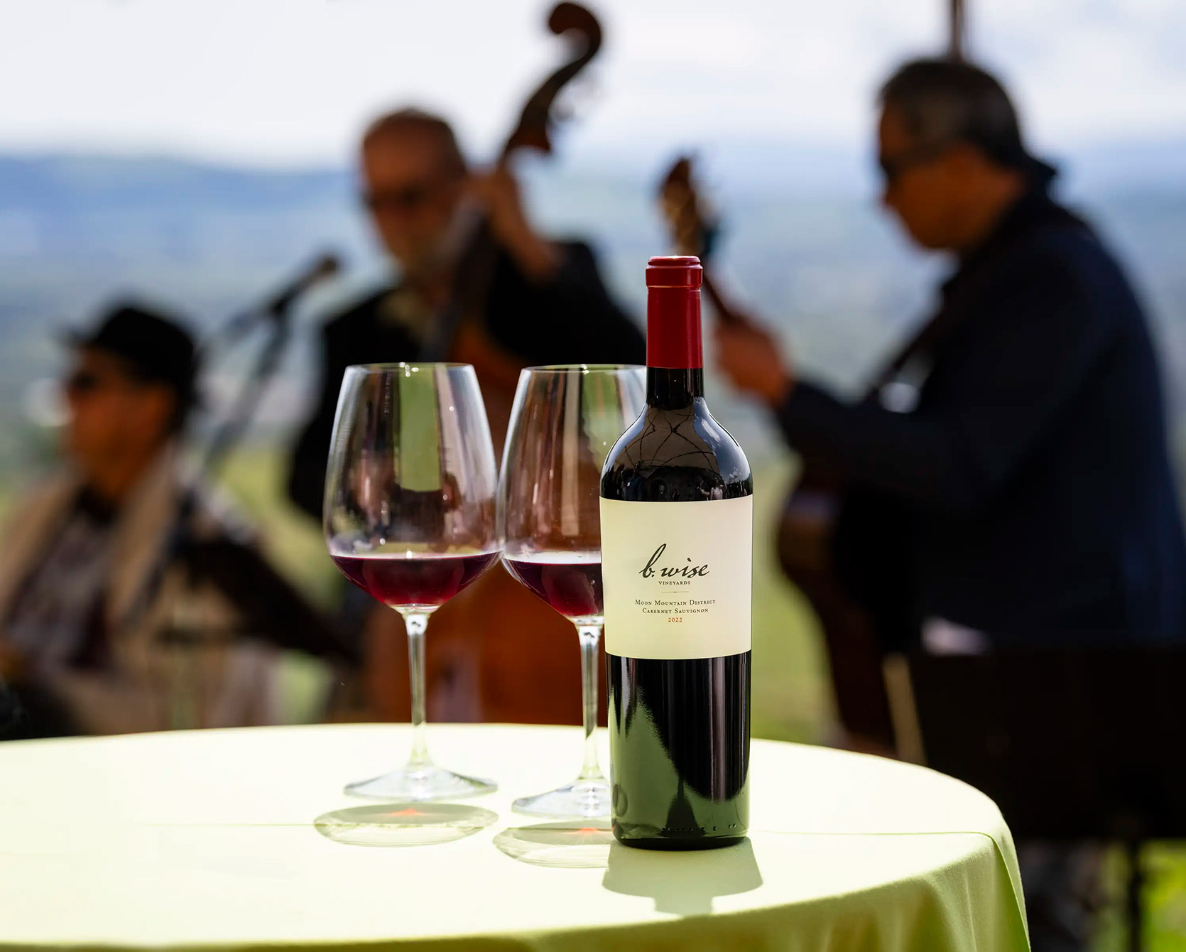 b. wise club patio party with bottle of wine and glasses in the for ground and musicians in the background